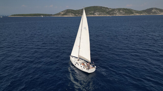 Croatia - 22 August 2023: Aerial view of a white sailboat with people on deck navigating the blue Adriatic Sea near the islands of Hvar.