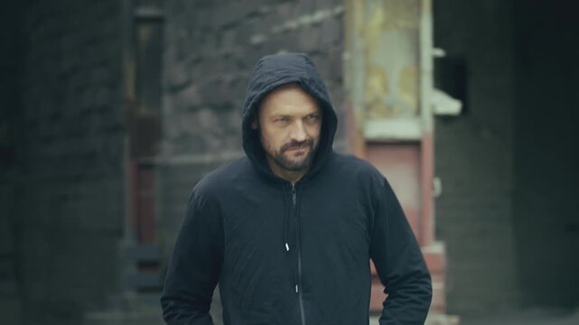 Suspicious hooded man walking alone at abandoned industrial site, crime concept