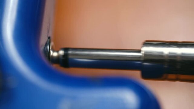 Extreme close up shot of male hand unplugging shiny metal audio jack connector from blue electronic device socket, disconnecting sound transmission cable from music equipment.