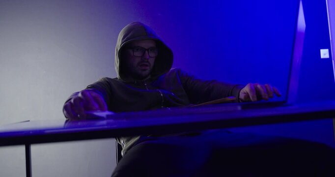 Hooded Hacker Working on Laptop During Cyber Attack in Blue Neon Light