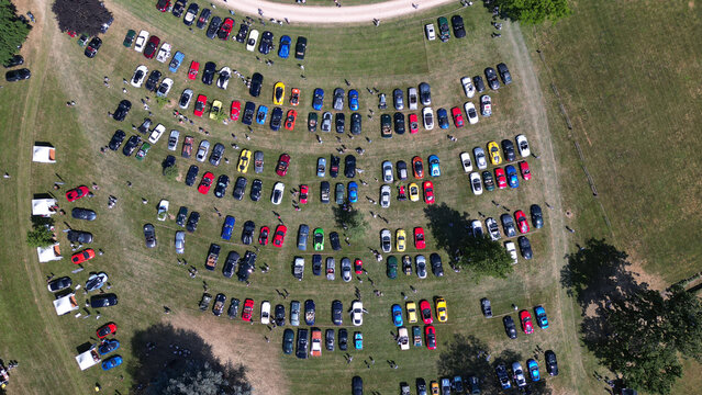 Francheleins, France - 04 June 2023: Aerial view of a car show at Chateau de Vataneins with rows of colorful vehicles parked on the grass and people walking around.