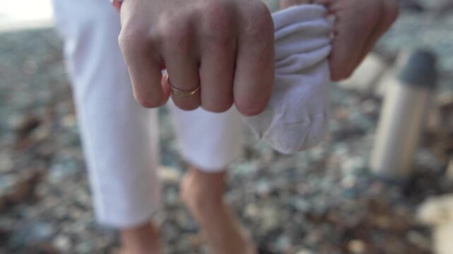 Sock, woman, beach putting on white socks to protect her feet while standing on a cold, pebbled shore outdoors.