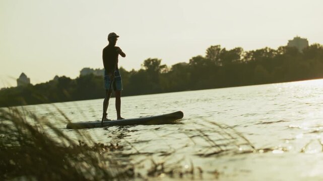 Surfer Riding Stand Up Paddle Board On River At Sunset. Summer Sports Recreation