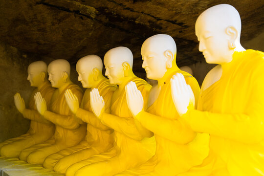 View of a row of Buddhist monk statues in yellow robes with hands in prayer position inside a cave at Adam's peak Ratnapura, Sabaragamuwa Province, Sri Lanka.