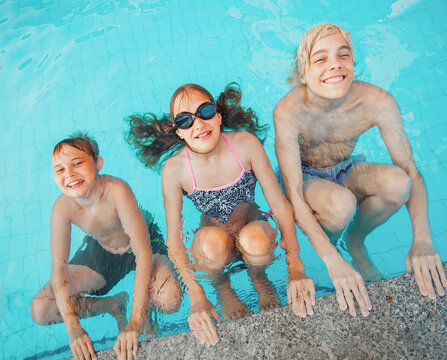 Kids having fun in swimming pool. Group of boy and girl playing in water. Happy children on summer vacation enjoying outdoor activity at resort. Aquatic leisure lifestyle concept.
