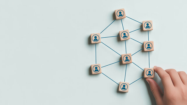 A person's hand connects wooden blocks with person icons in a complex network, symbolizing interconnectedness, networking, and strong business relationships.