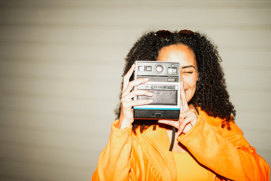 Young afro hair woman using vintage old instant photo camera outdoor - Girl having fun with analog tool - New trends and young people lifestyle concept - Main focus on hands - Flash UGC content