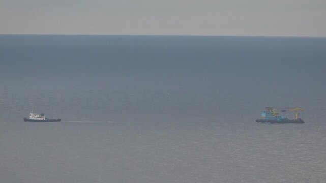 Tugboat, Barge, Ocean pulling heavy crane platform across the vast, calm gray sea horizon.