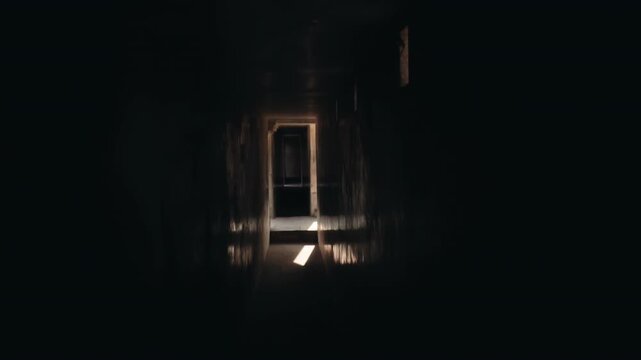 Mysterious and creepy perspective moving forward in a dark, scary, and abandoned building corridor, with a glimpse of hope represented by a ray of sunlight at the end of the tunnel