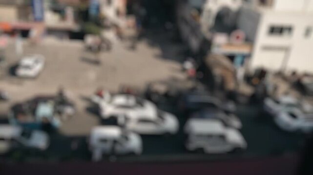 Defocused aerial view of a bustling city street with heavy traffic, showing cars, motorcycles, and buses moving through a congested intersection in an urban environment during the daytime