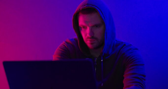 Hooded Man Using Laptop in Neon Light Cybersecurity Concept