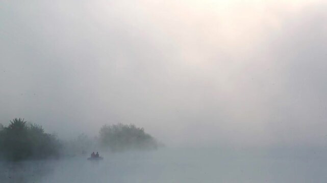 Two people in a boat in a lake, fishing at sunrise, with fast-moving vapor and clouds