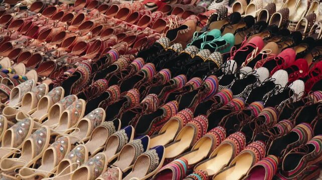 Colorful handmade traditional Indian shoes, known as jutti or mojari, are neatly arranged for sale at a bustling outdoor market stall, showcasing intricate designs and vibrant leather craftsmanship