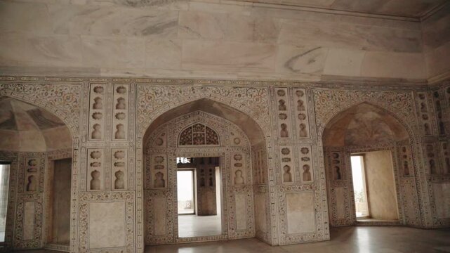 Elegant interior of a historic palace hall inside the famous Agra Fort in India, showing detailed mughal architecture with intricate carvings, arched windows, and beautiful white marble walls