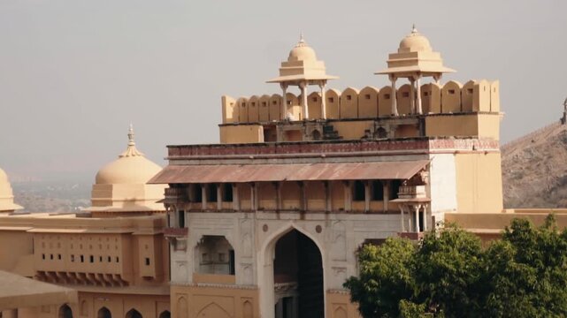 Majestic amber-colored walls of the Amer Fort and Palace, a historic landmark in Jaipur, Rajasthan, showcasing ancient Indian architecture against a hazy sky with surrounding hills