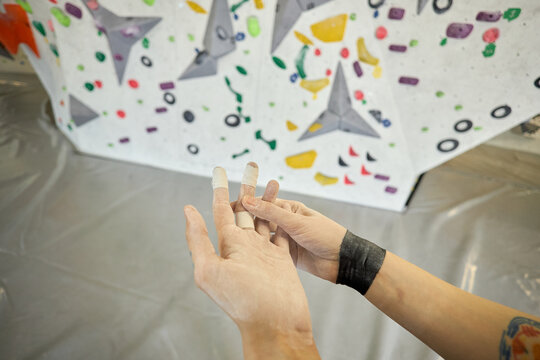 Close up of young adult climber taping fingers and preparing hands before bouldering wall session, showing fitness training and grip care for sports marketing or gym promotion