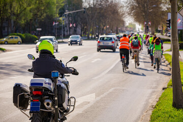 Fototapeta premium Police officer on motorcycle secures group of cyclists on city road, street, asphalt