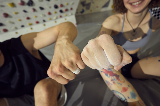 Young adult climbers bumping chalked fists after training session at indoor bouldering gym, showing teamwork and active lifestyle