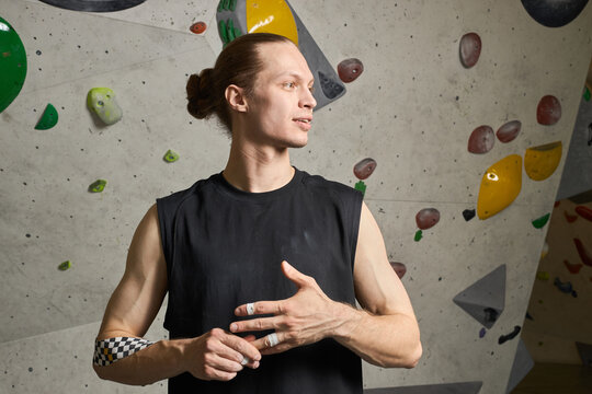 Young adult Caucasian man preparing for bouldering, taping fingers and standing by climbing wall, conveying fitness training and active lifestyle