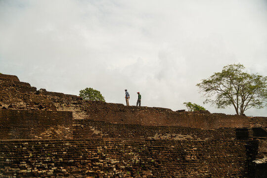 View of the ancient stone ruins of Sigiriya fortress with two people standing on the historic walls under a cloudy sky Sigiriya, Central Province, Sri Lanka.