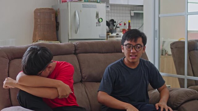Younger brother sad or defeated older sibling during an emotional conversation on living room sofa