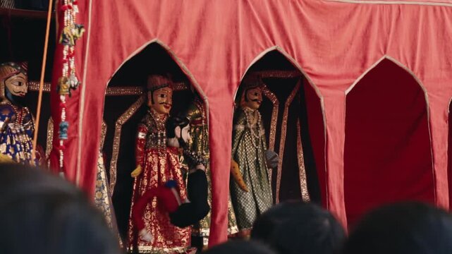 Colorful handmade Rajasthani puppets, known as Kathputli, performing a traditional folk story on a decorated stage with red curtains for an engaged audience during a cultural festival