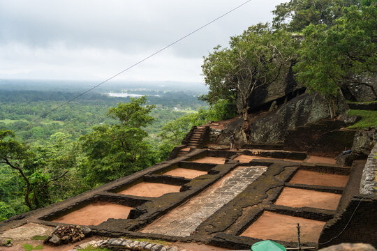 View of the ancient stone foundations and ruins of Sigiriya rock fortress overlooking the lush tropical jungle under an overcast sky Sigiriya, Central Province, Sri Lanka.