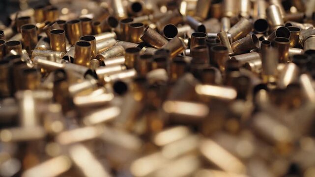 Macro close-up of a large pile of shiny brass spent bullet casings falling in slow motion, representing concepts of conflict, war, violence, and ammunition manufacturing