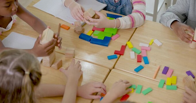 Elementary children place colorful blocks into pattern on wooden desk during group learning activity, back to school teamwork builds problem solving, math readiness, communication, cooperation