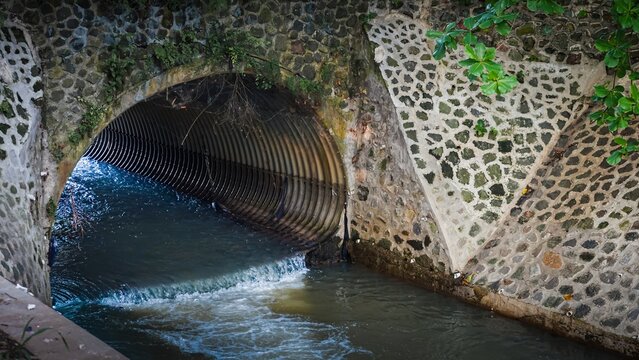 Water flowing through corrugated metal pipe culvert under stone bridge