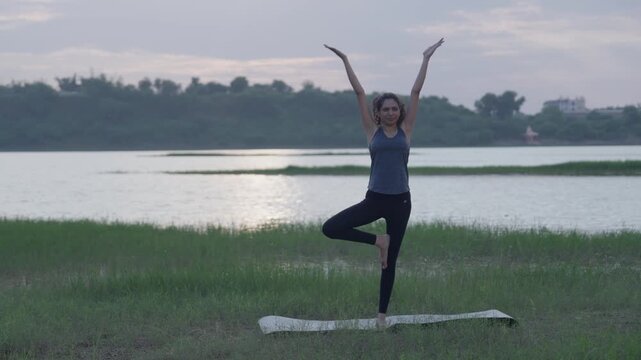 A slow-motion of a South Asian Woman in backbend doing yoga by a calm lake at twilight