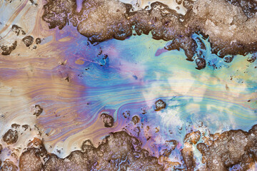 Fototapeta premium Iridescent oil slick patterns bloom on melting snow and muddy ground, reflecting the vibrant colors of spring pollution in a waterway