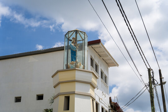 View of the statue of Our Lady of Matara in a glass enclosure atop a white building under a blue sky with clouds in Matara, Southern Province, Sri Lanka.