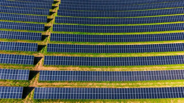 Top down aerial view of geometric industrial solar panel rows. Directly overhead zenith view of parallel rows of solar panels over green grass.