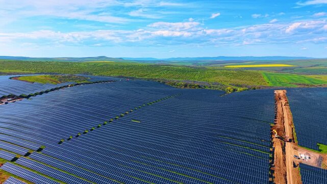 Expansive industrial solar farm installation with dirt access roads. High angle perspective of wide solar panels grid divided by construction paths and vehicles.