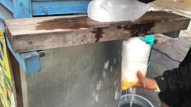 A person is using a manual ice shaver to create shaved ice for es teler and es campur.