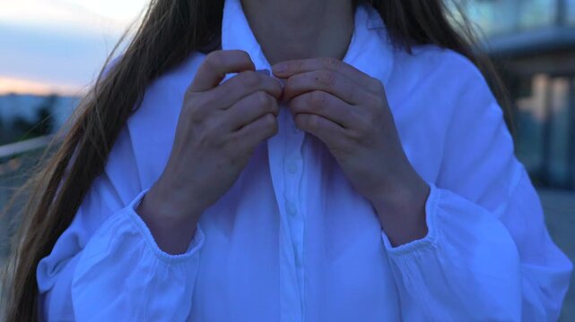 Woman blouse buttoning close up of person fastening white shirt on terrace at dusk