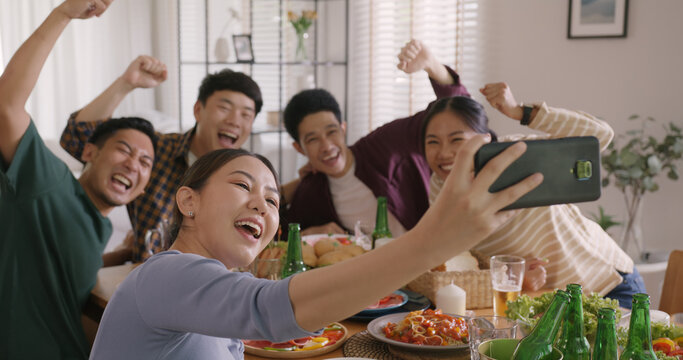 Happy hour diner at home relax smile look at camera shooting video photo on mobile app. Group of asia people young adult friend man and woman sit at dining table joy fun talk or eat food drink beer.
