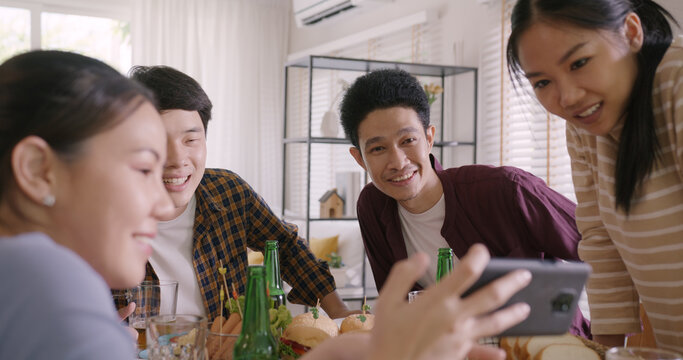 Happy hour diner at home relax smile look at camera shooting video photo on mobile app. Group of asia people young adult friend man and woman sit at dining table joy fun talk or eat food drink beer.