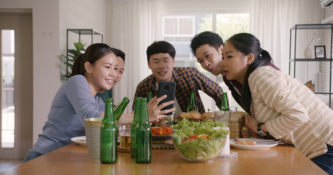 Happy hour diner at home relax smile look at camera shooting video photo on mobile app. Group of asia people young adult friend man and woman sit at dining table joy fun talk or eat food drink beer.