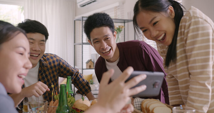 Happy hour diner at home relax smile look at camera shooting video photo on mobile app. Group of asia people young adult friend man and woman sit at dining table joy fun talk or eat food drink beer.