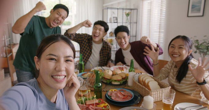 Happy hour diner at home relax smile look at camera shooting video photo on mobile app. Group of asia people young adult friend man and woman sit at dining table joy fun talk or eat food drink beer.