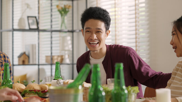 Happy hour good warm summer time diner indoor home. Group of asia people young adult friend man and woman sit at dining table joy fun talk or eat food and drink beer alcohol bottle glass inside house.