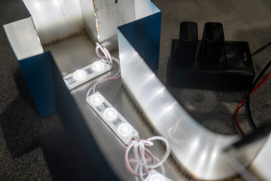 Close-up of illuminated blue acrylic channel letter signage with LED lighting during fabrication process in a signage workshop