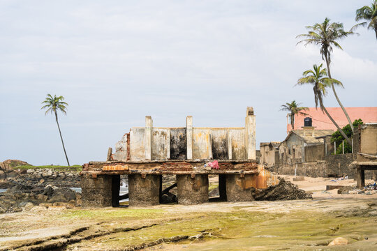 View of a ruined coastal building with weathered concrete walls and palm trees on a rocky beach in Galle, Southern Province, Sri Lanka.