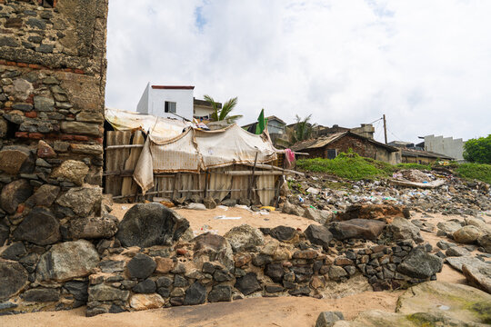 View of makeshift shelters and stone walls along a rocky coastal area under a cloudy sky in Galle, Southern Province, Sri Lanka.