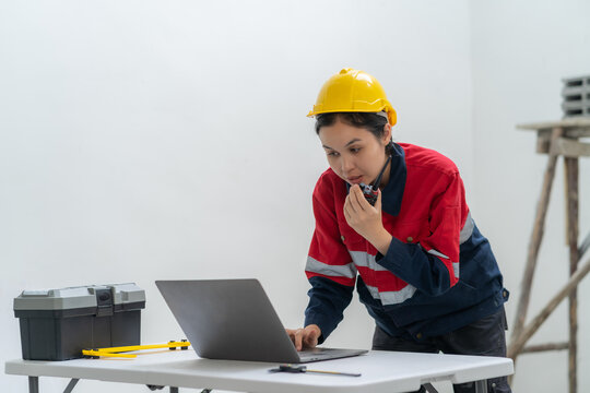 Professional contractor using laptop computer and talking on walkie-talkie radio at desk with toolbox during interior project inspection inside residential house construction site