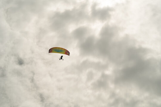 View of a powered paraglider with a colorful wing soaring through a dense layer of grey overcast clouds in Sri Lanka.