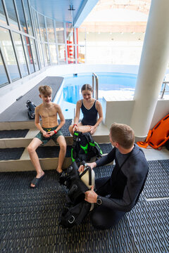 Diving instructor explaining scuba equipment with an oxygen cylinder to a boy and a girl during a pool lesson