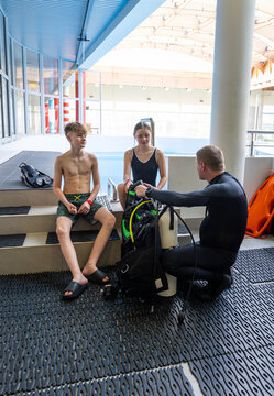 Diving instructor explaining scuba equipment with an oxygen cylinder to a boy and a girl during a pool lesson